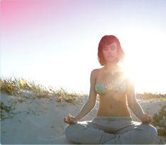 Imagem de uma mulher sentada na praia, a meditar. A imagem ilustra que é possível descontrair e viver normalmente, mesmo quando está com o período.